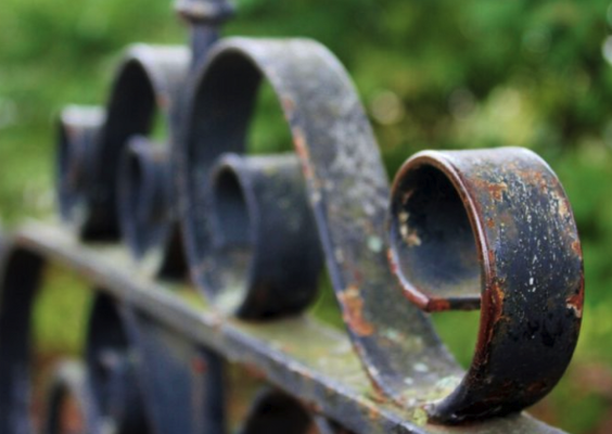 Close-up of an old, rusty metal railing with decorative curved patterns. Soft, green background out of focus.